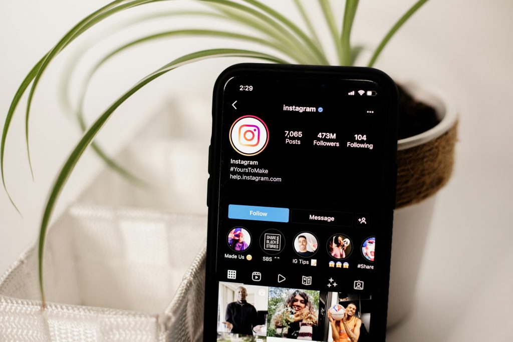 Smartphone con instagram aperto sllo schermo, appoggiato su un tavolo accanto a una pianta in vaso